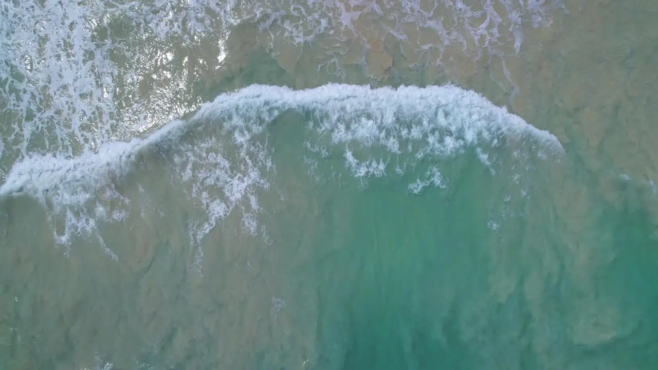 Vertical aerial ascent over shallow white sand beach with calm turquoise waters in Oahu Hawaii