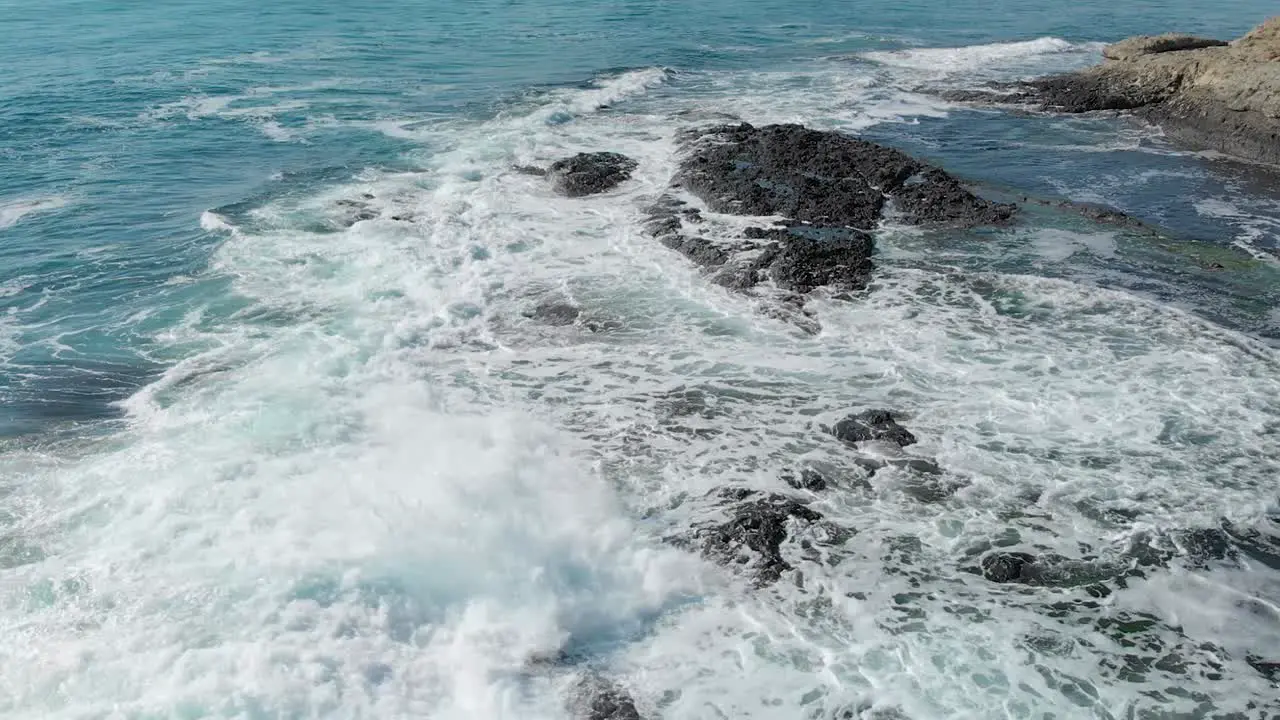 Turquoise waves rolling over black rock -aerial