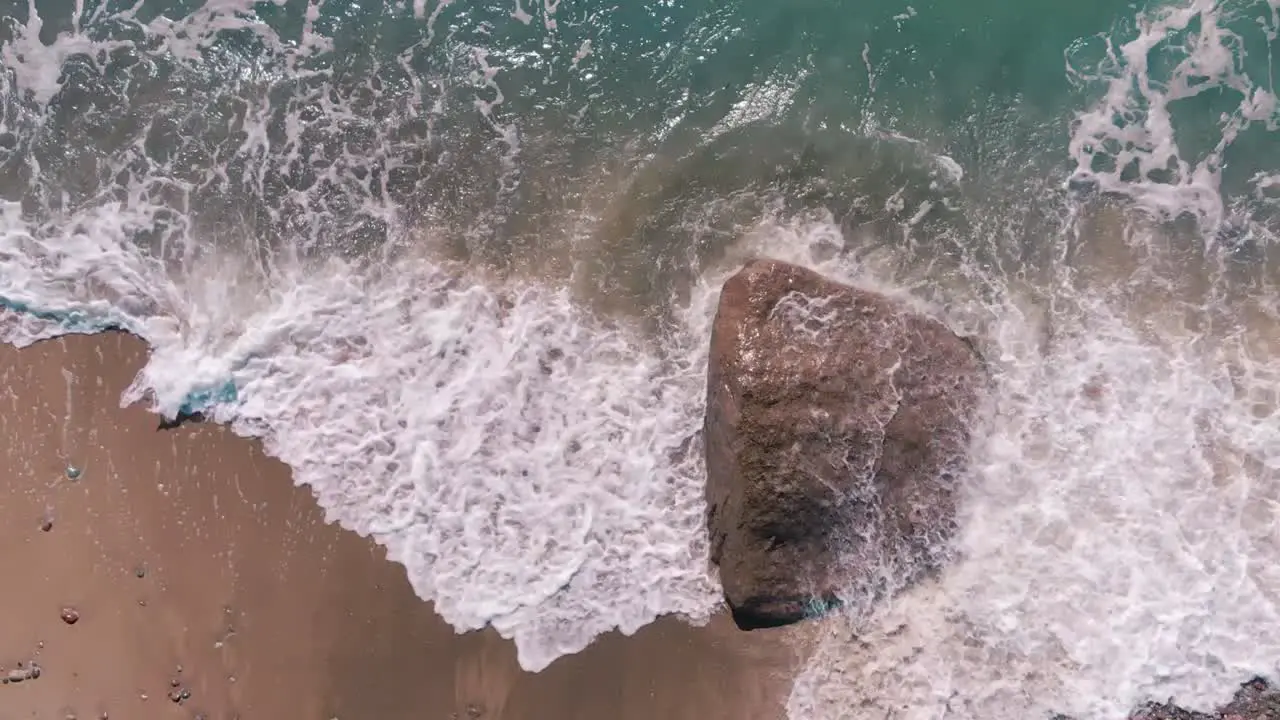 Large stone is hit by Baltic Sea foamy waves top down view