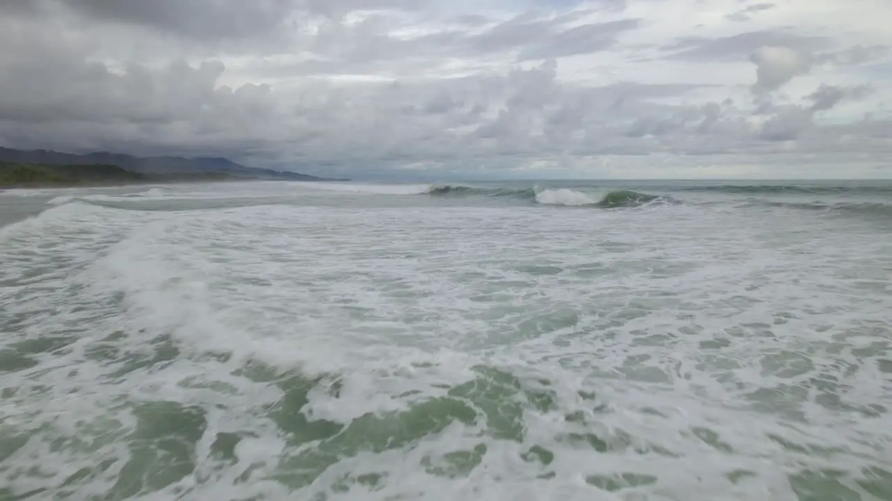 Aerial dolly in of turquoise foamy sea waves near the coastline on a cloudy day in Dominicalito Beach Costa Rica