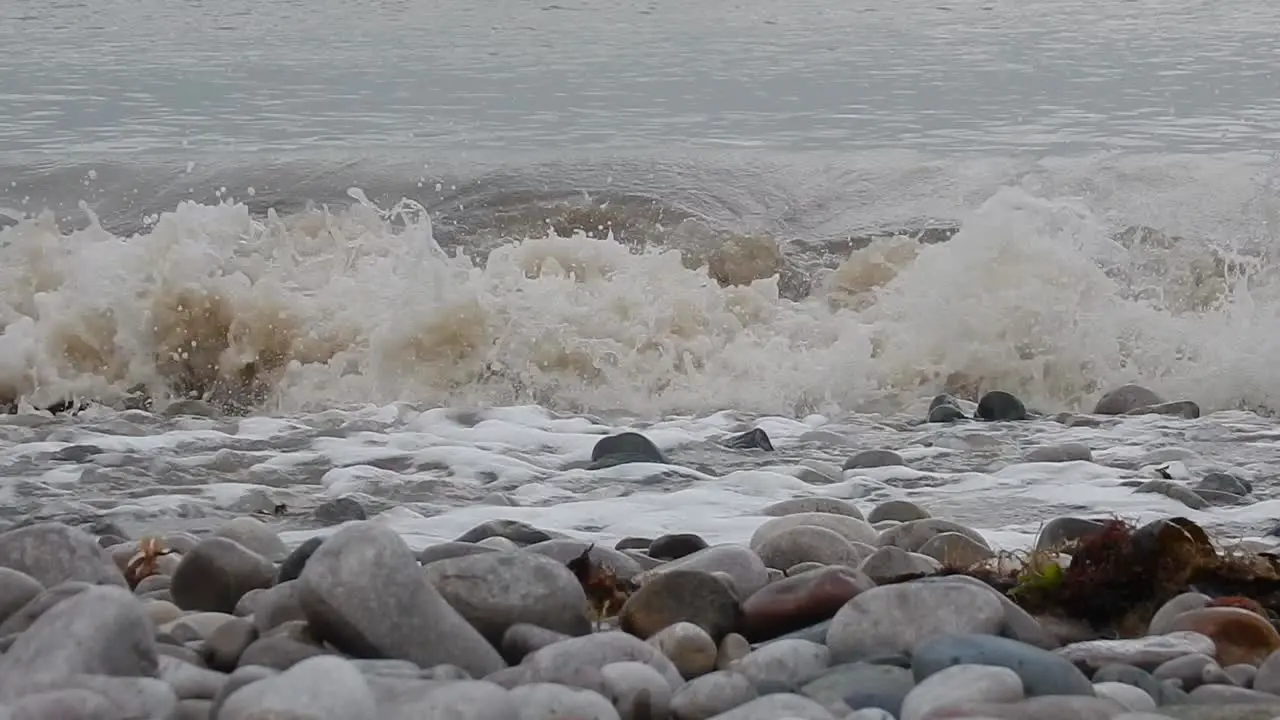 Foaming white waves washing into calming serene rocky pebble stone shoreline