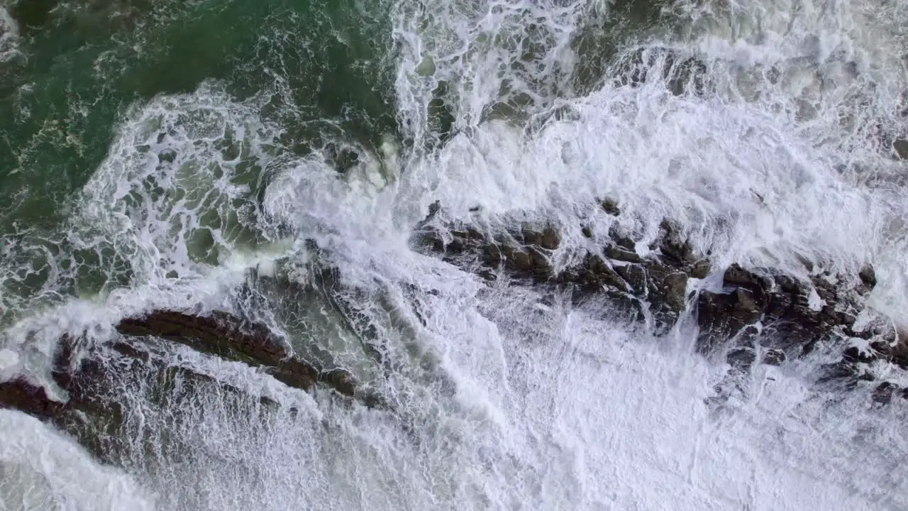 Aerial rising over turquoise foamy sea waves in rocky shore covered in vegetation in Dominicalito Beach Costa Rica