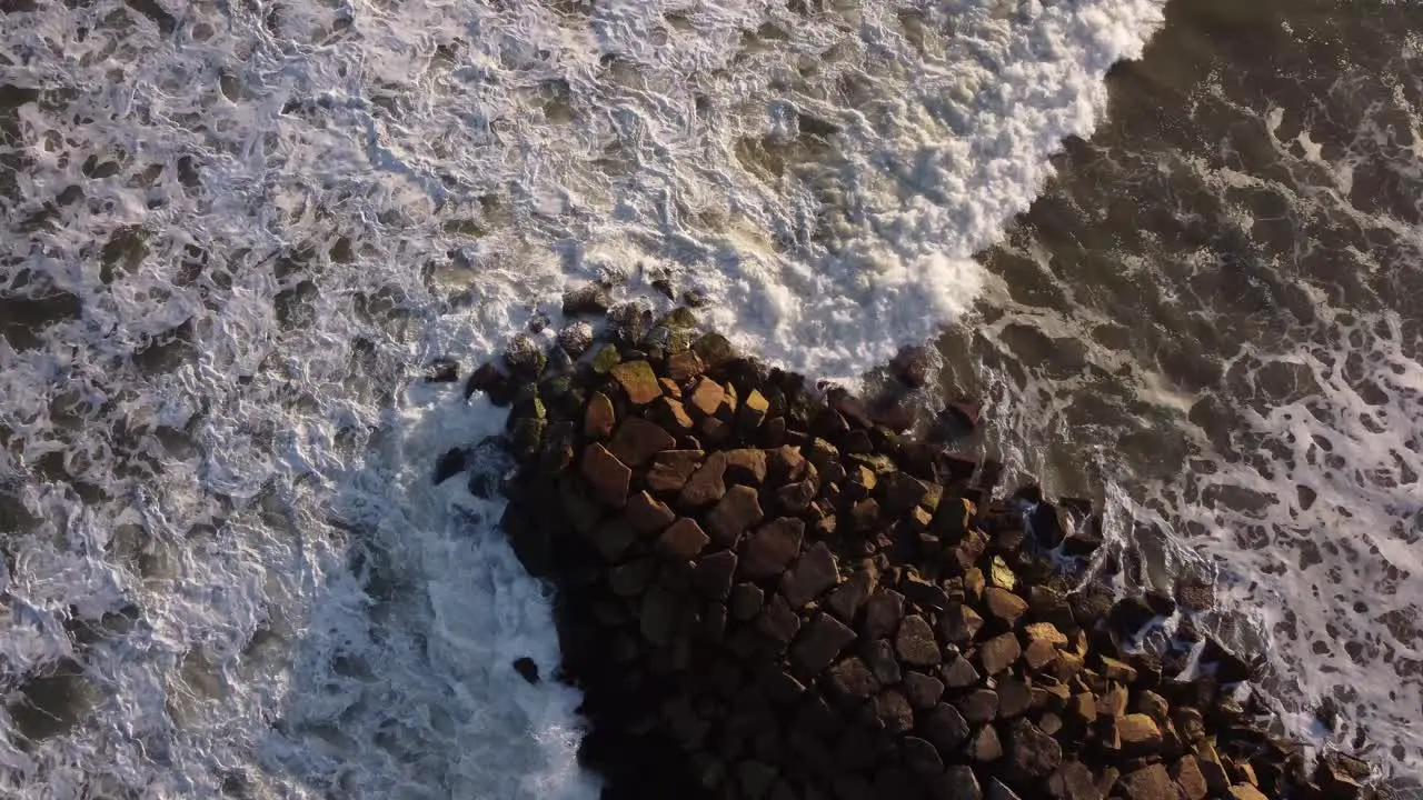 Aerial top down shot of stormy waves of ocean crashing against rocky jetty during sunset Circle shot