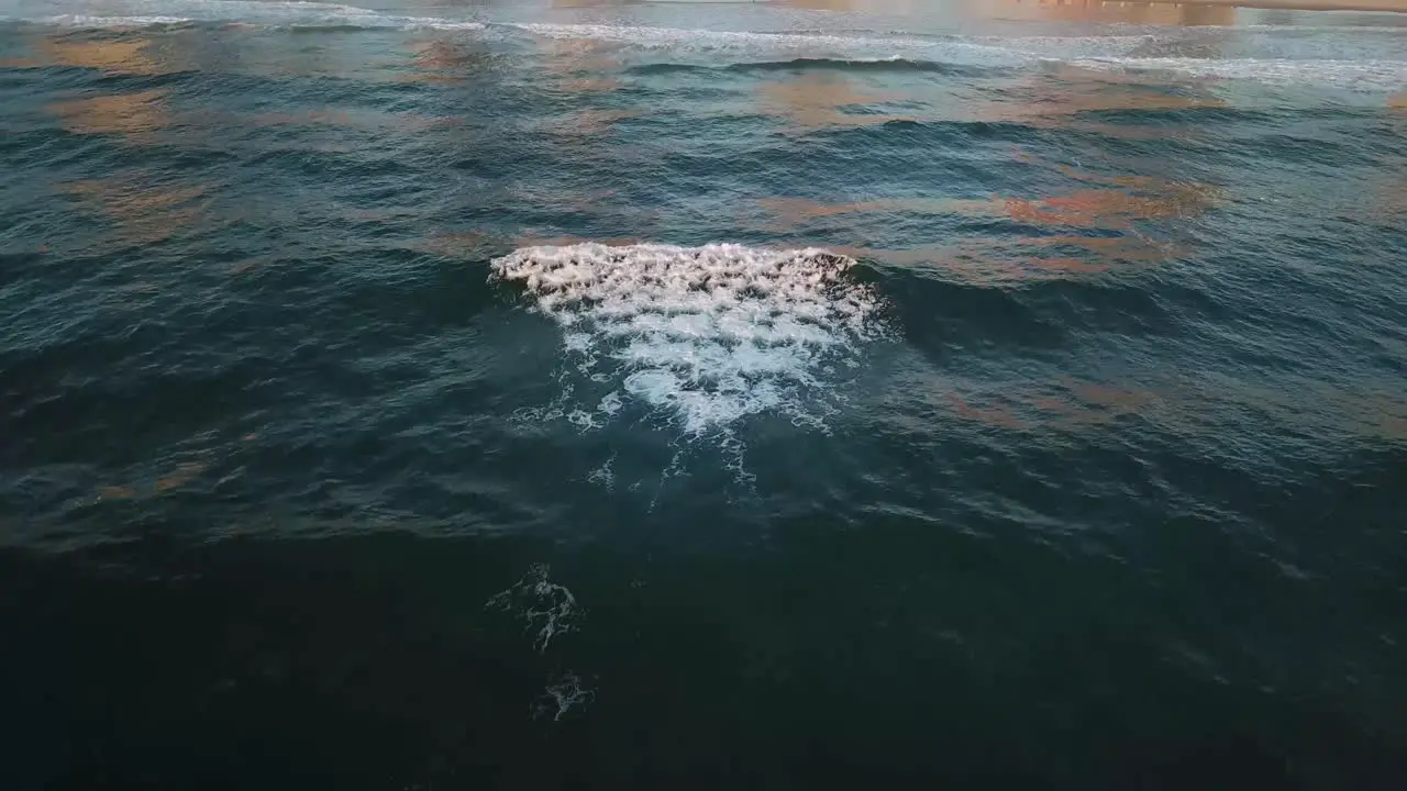 Drone aerial shot during sunrise over waves with people walking on beach