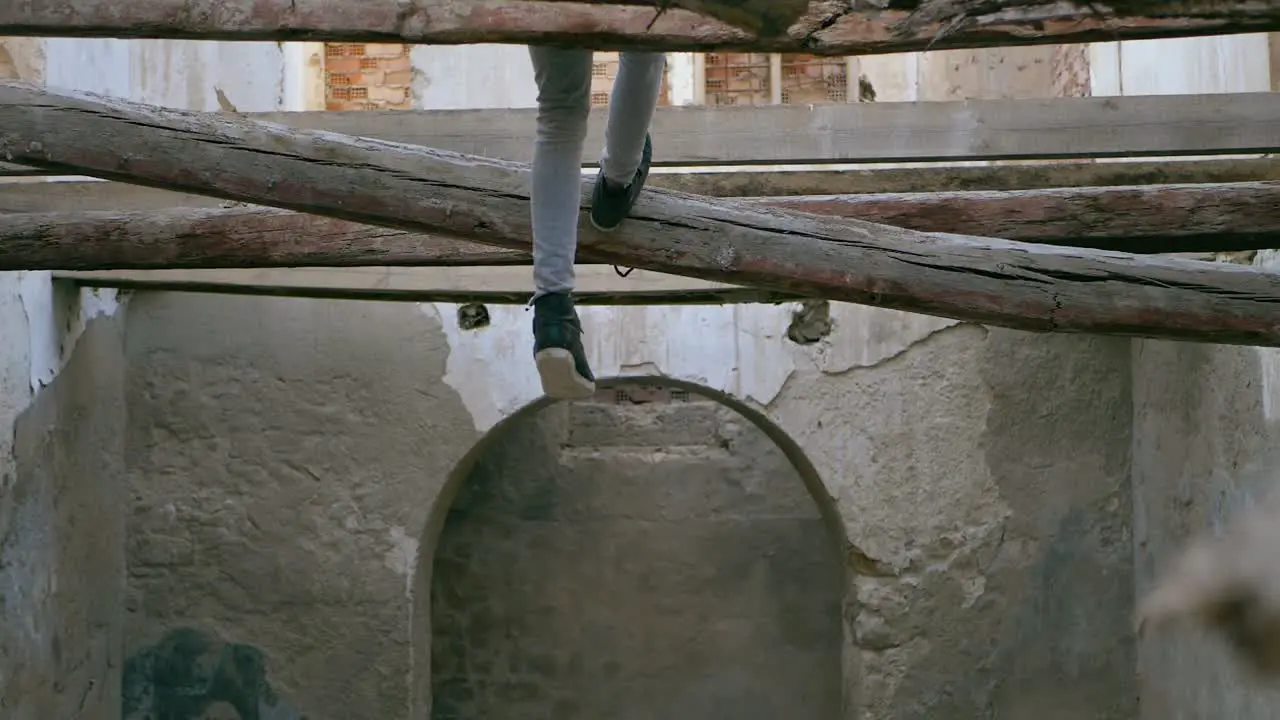 Young man teenager swings his feet sitting several meters high on a collapsed beam in an abandoned house