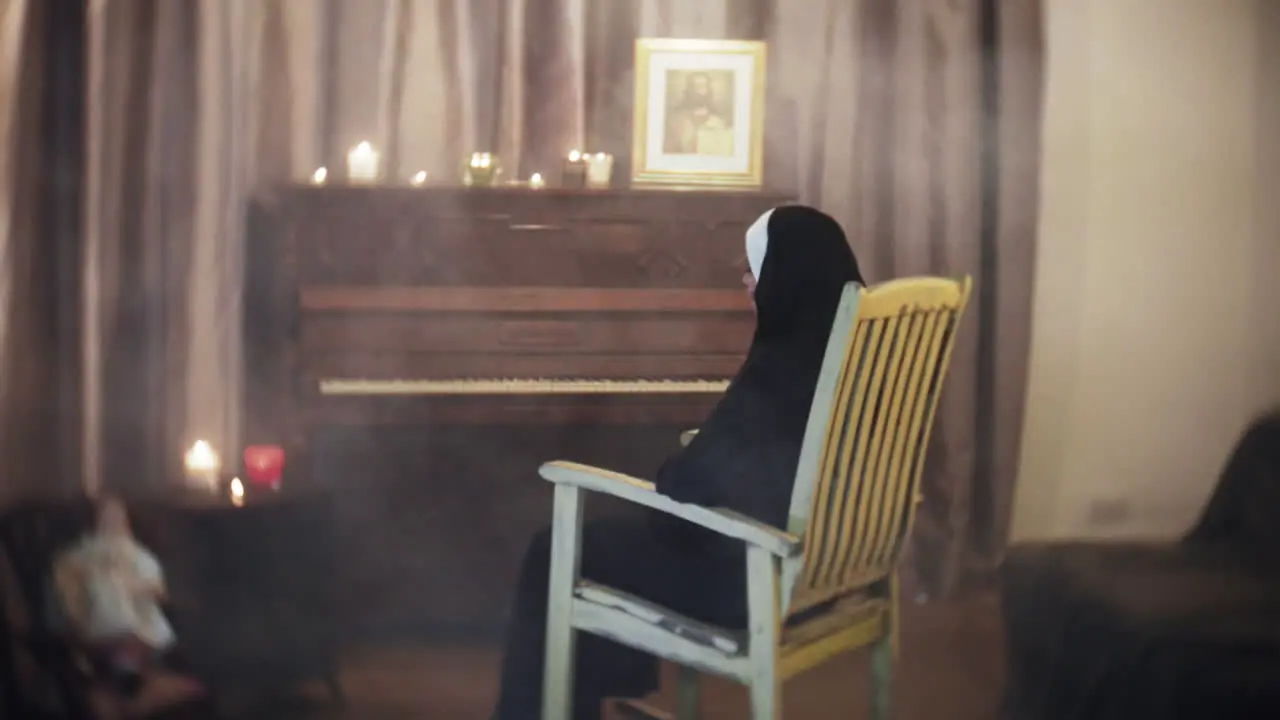 Spooky creepy Nun in a horror scene rocking in a rocking chair in a living room with a piano a doll and candles