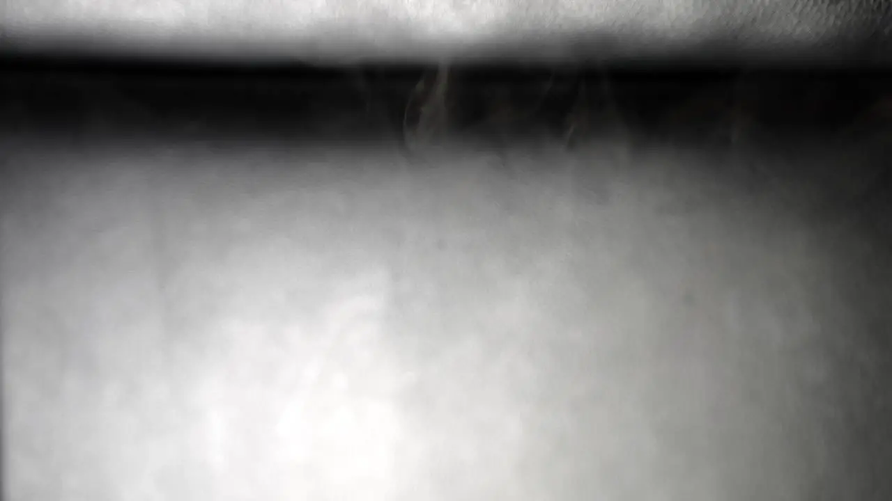 Wispy tendrils of smoke drop slowly from top to bottom in slow motion