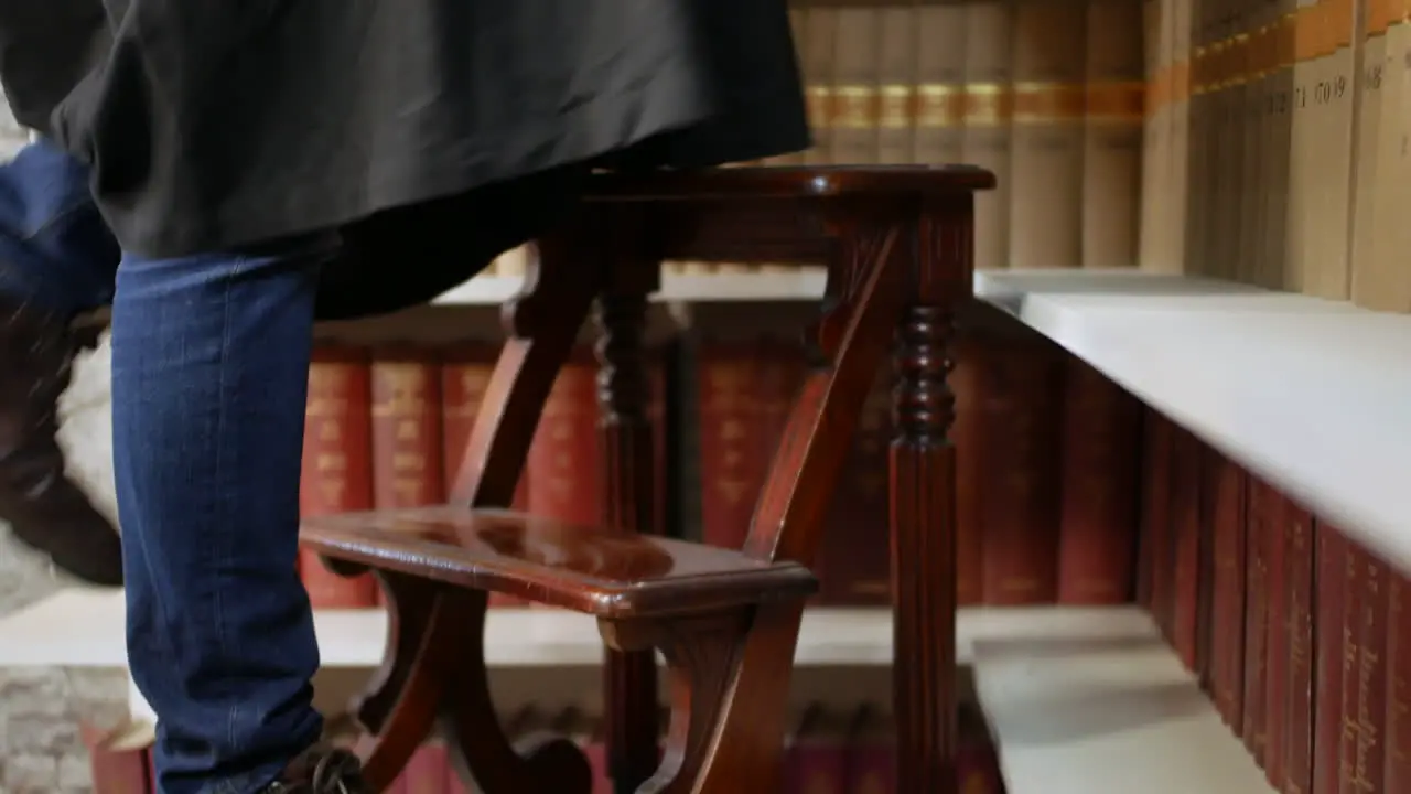 A student climbing library ladders steps to reach books on a high shelf in a judges law library