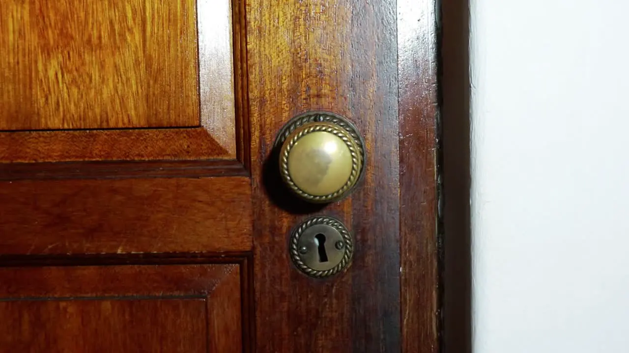 Door knob turns and man with black glove opening wooden door slowly