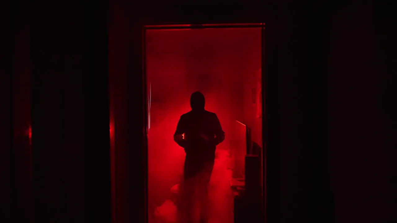 Slow motion zoom of evil shadowy figure holding knife in glowing red fog