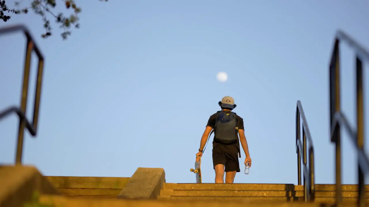 Teen Walking With Skateboard With Moon In The Sky