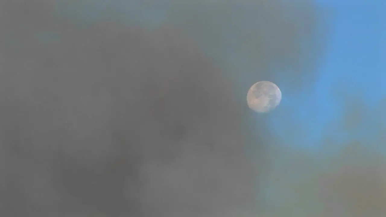 Long Shot Of Clouds Of Dark Smoke Clearing To Reveal The Moon In A Blue Sky