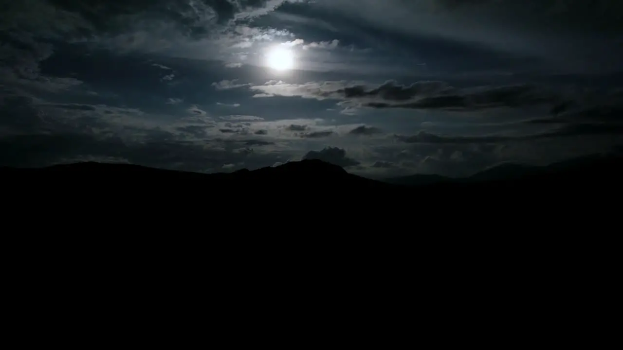 Hyperlapse of full moon at a cloudy night with dark silhouette of mountains