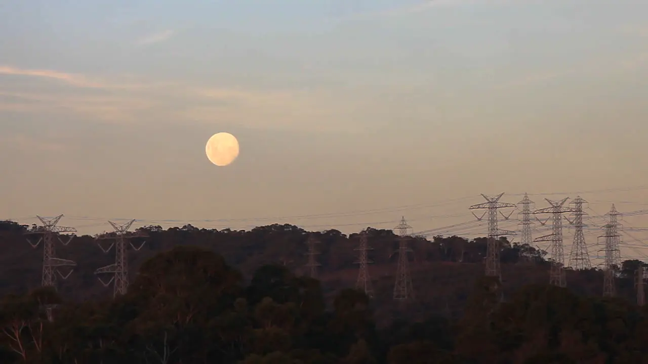 Full moon sitting above silhouetted power lines above providing power to surrounding suburban areas