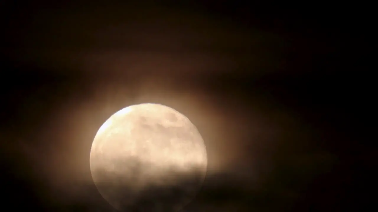 Nighttime closeup of full moon rising while being enveloped by ominous clouds