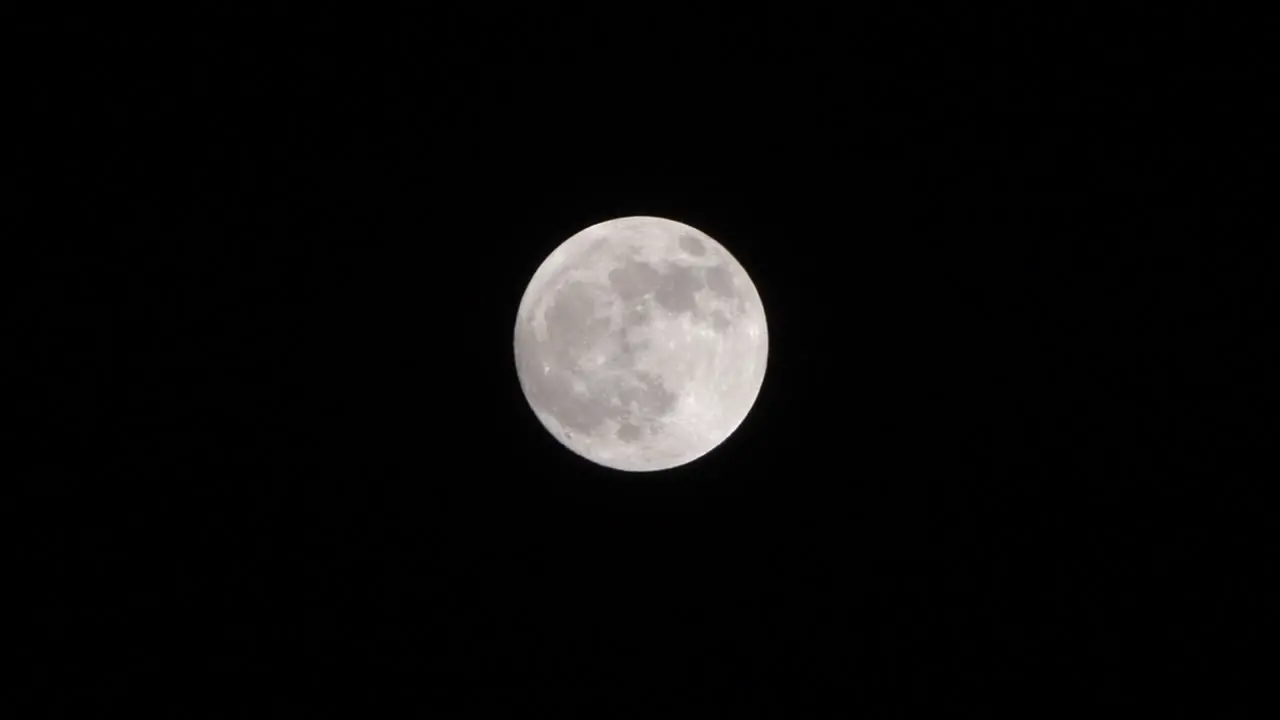 Close up shot of full moon set against dark black night sky in slow motion