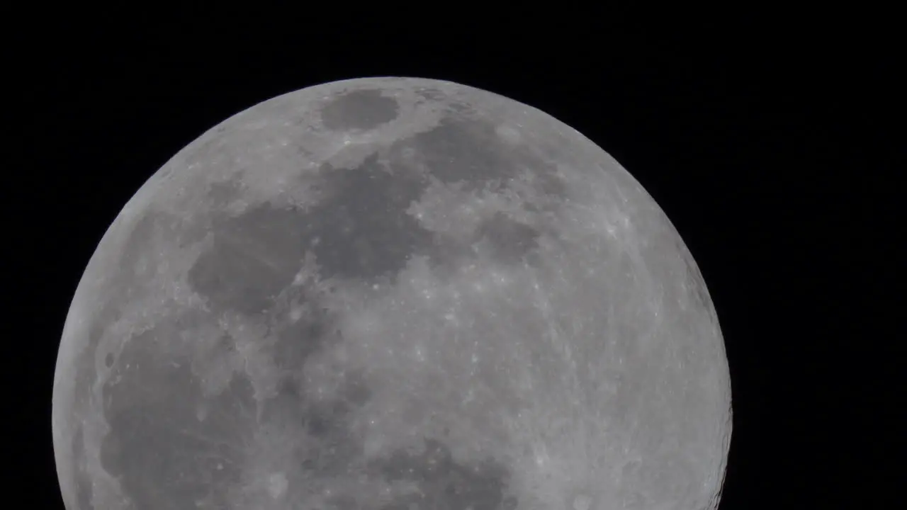 Super zoom or telescope view of the full moon crossing the night sky with crater and topography detail clearly visible time lapse