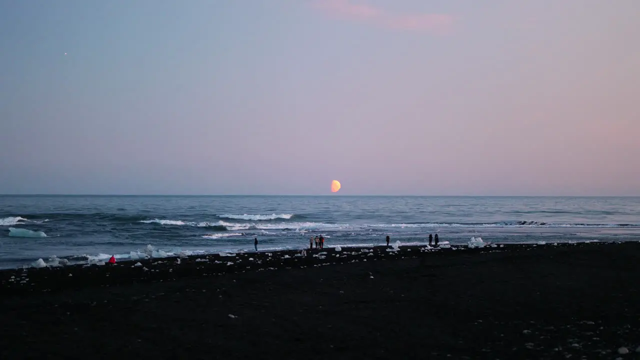 Extreme wide shot of people enjoying moonrise on Diamond Beach Iceland