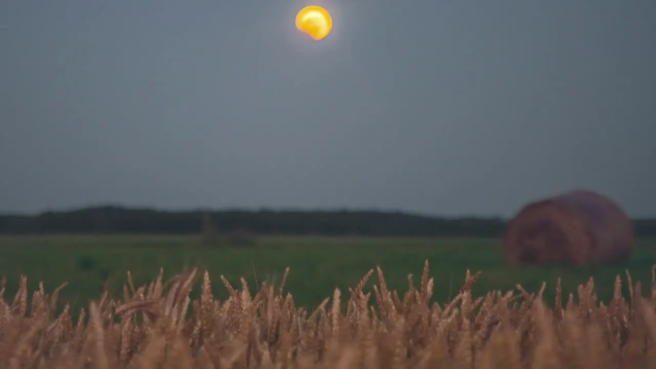 Time lapse of yellow moon descending on fields with bales of hay