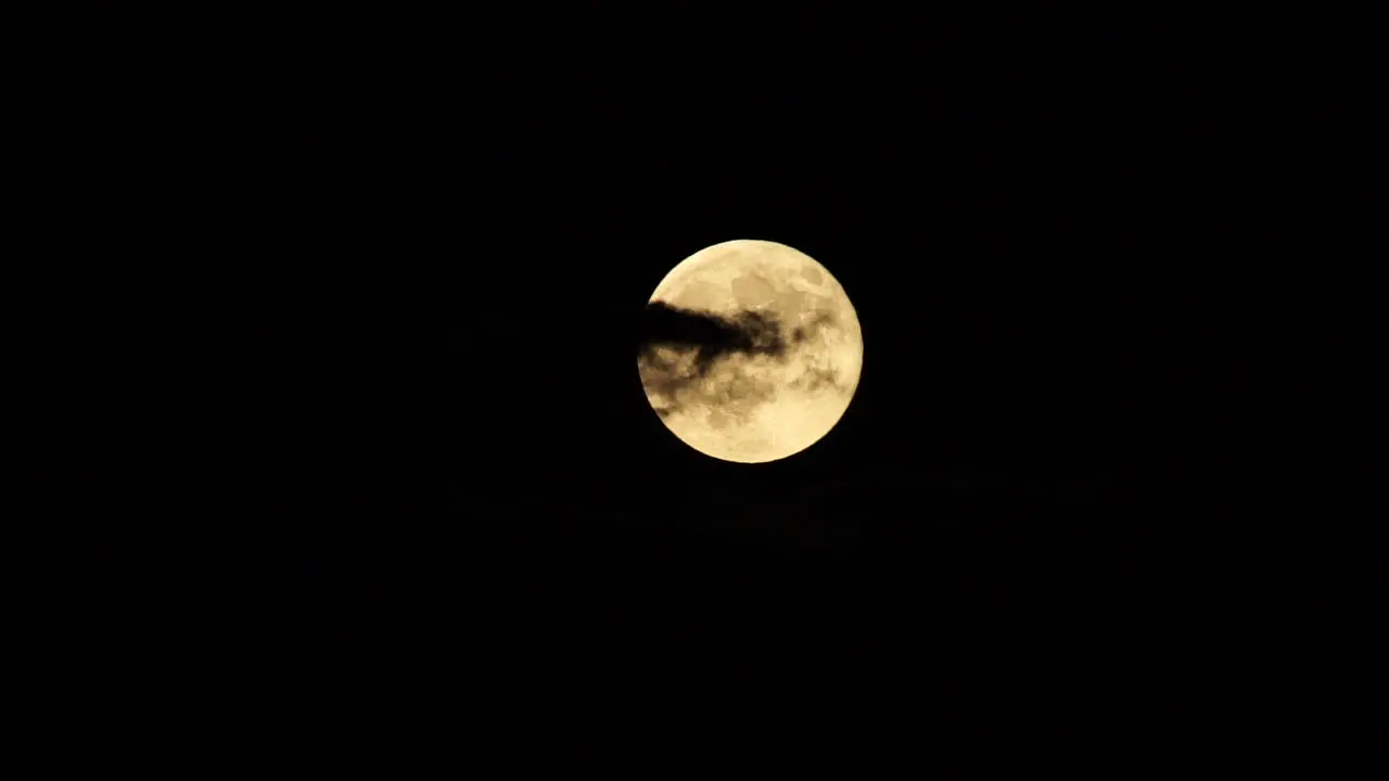 Full Moon rising behind clouds against dark sky