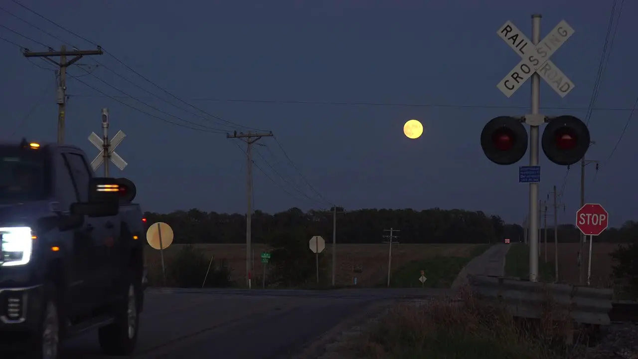 A Pickup Truck Crosses A Railroad Crossing With A Full Moon In The Distance At Night