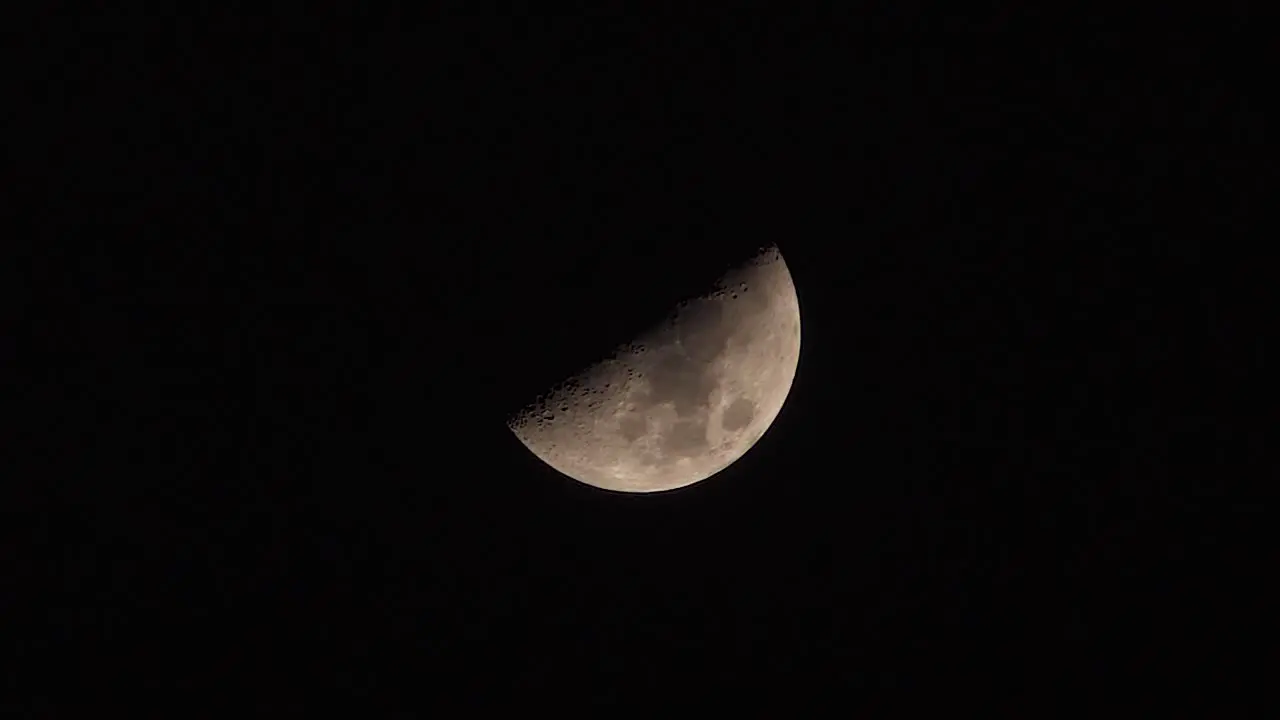 Half-moon slowly moving across a dark black night sky