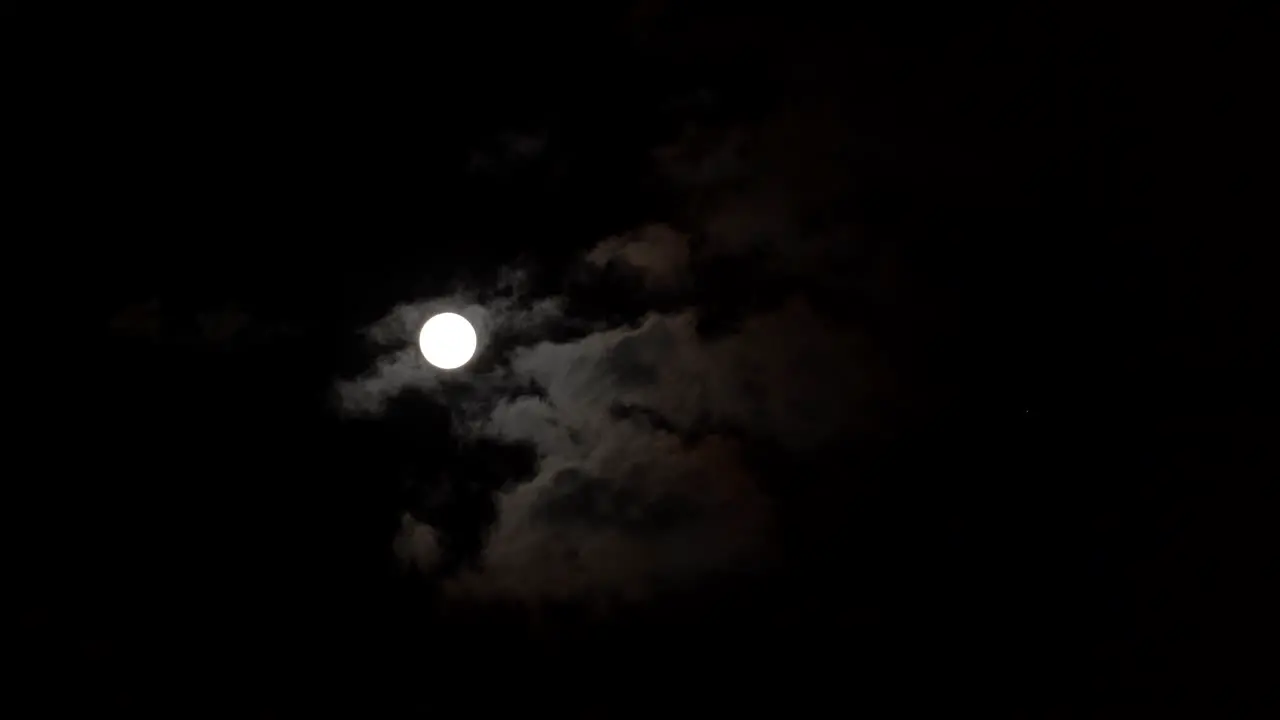 Moon glowing through clouds on dark night black sky timelapse