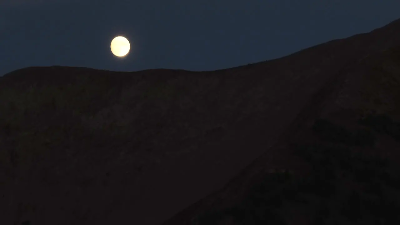 A full moon slowly disappears behind a ridge line in the Colorado Rocky Mountains in the middle of the night