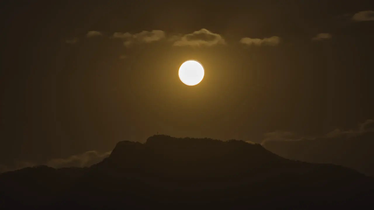 Night timelapse of a golden full moon rising over the top of a hill