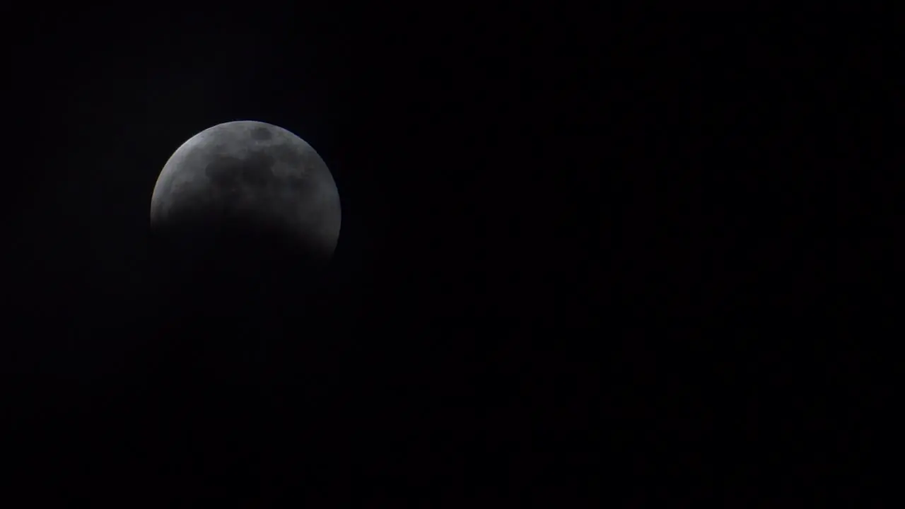 Thin clouds slowly reveal a full moon during a lunar eclipse