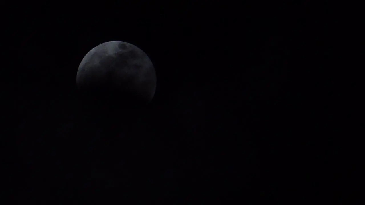 Clouds moving past a full moon in the middle of a lunar eclipse