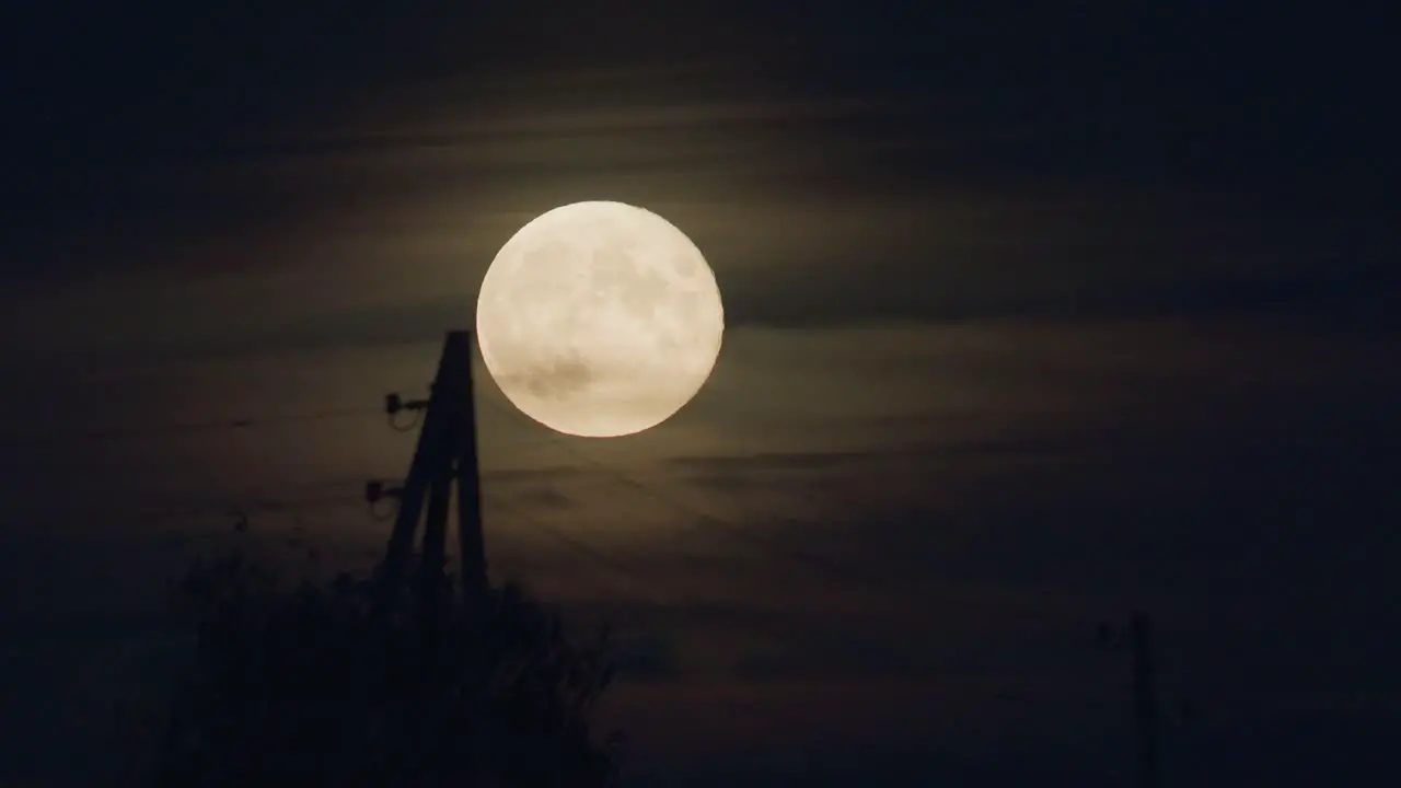 Dramatic low moon rise through thin cloud layer and electric pole time lapse strong air disturbance