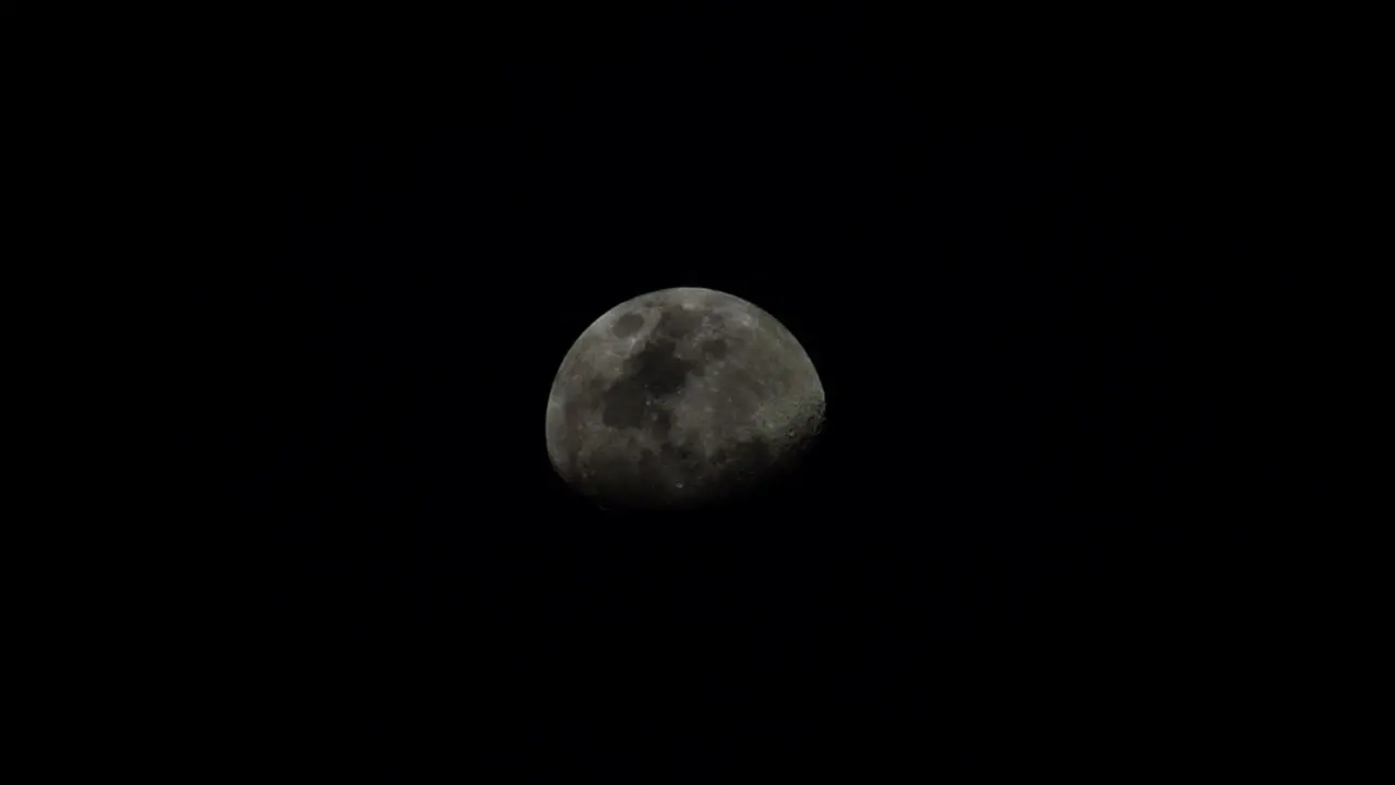 Waning gibbous moon ascending in a dark sky with wispy clouds passing by