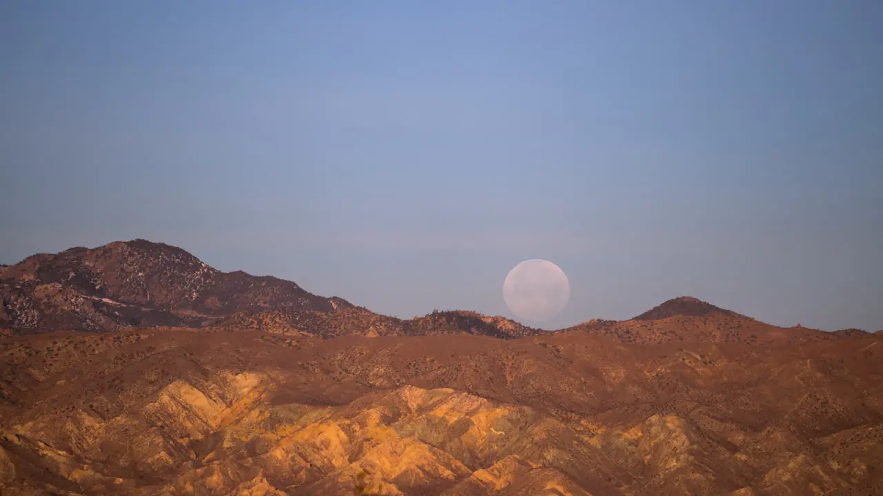 The full moon sets behind the rugged terrain in the Mojave Desert time lapse