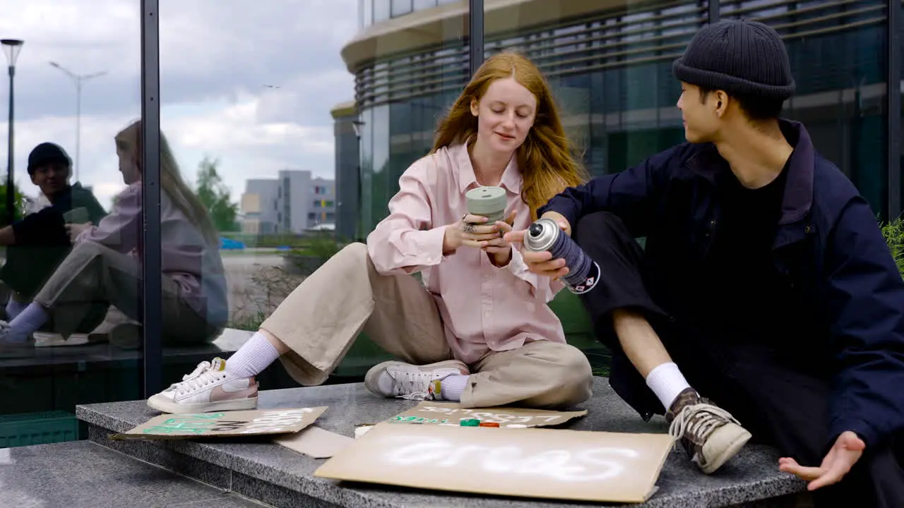 Ginger Woman Drinking Coffee While Man Painting Board For Protest