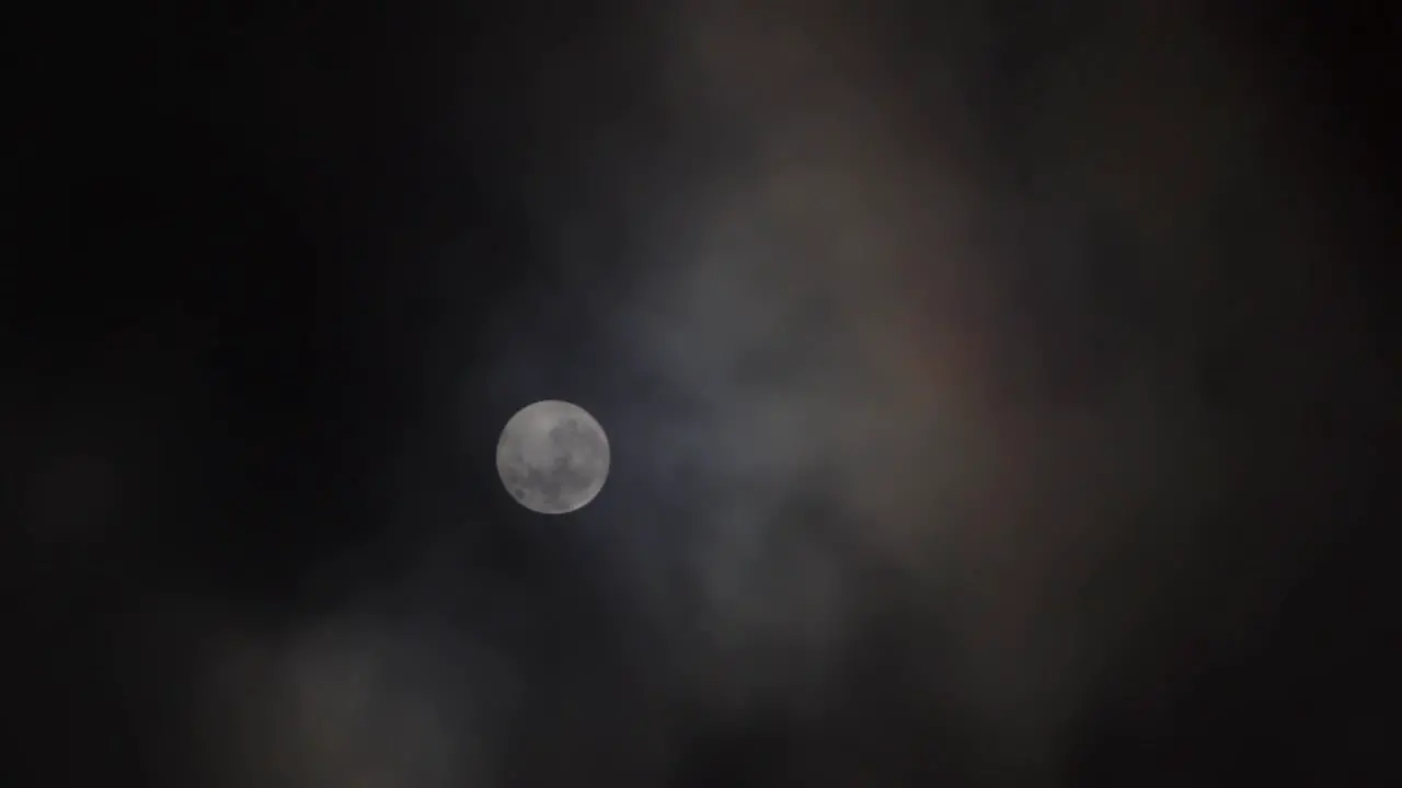 Clouds pass in front of Full Moon in a dark sky