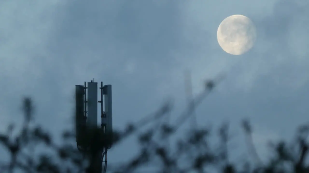 Cloud passing moon behind cellular telecommunication transmitter tower