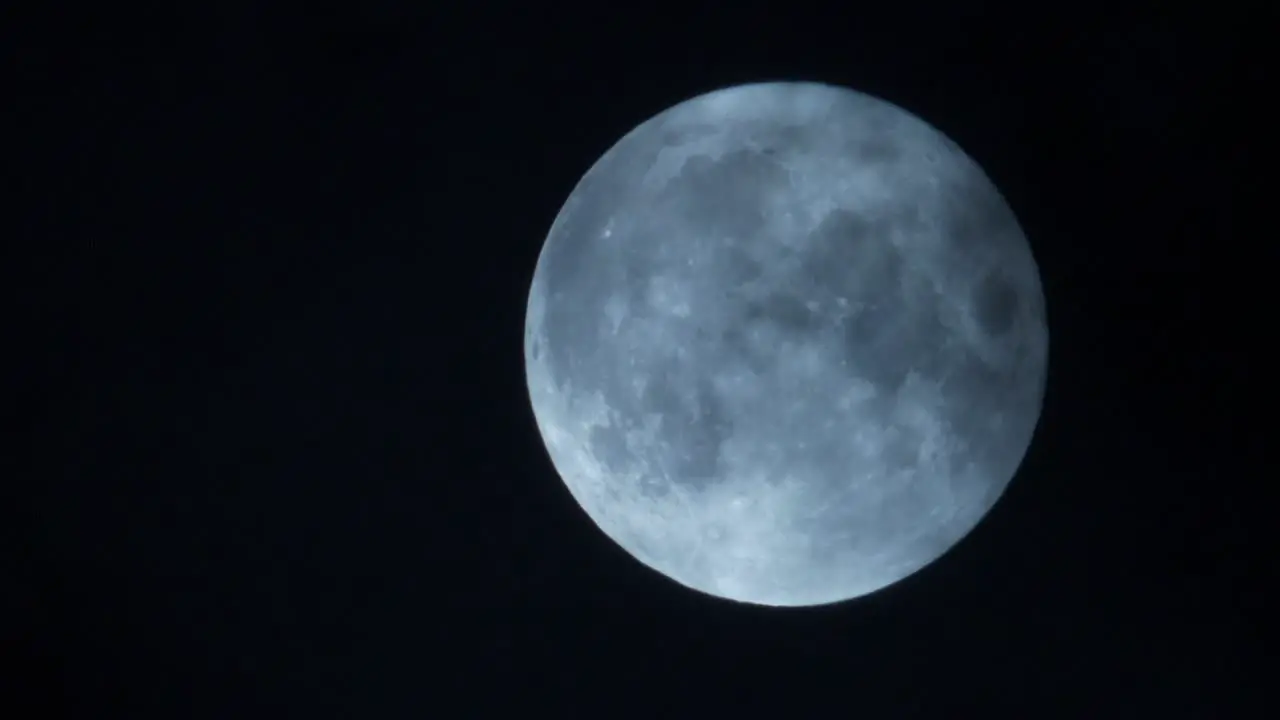 Magical full illuminated moon with clouds passing in night sky close up