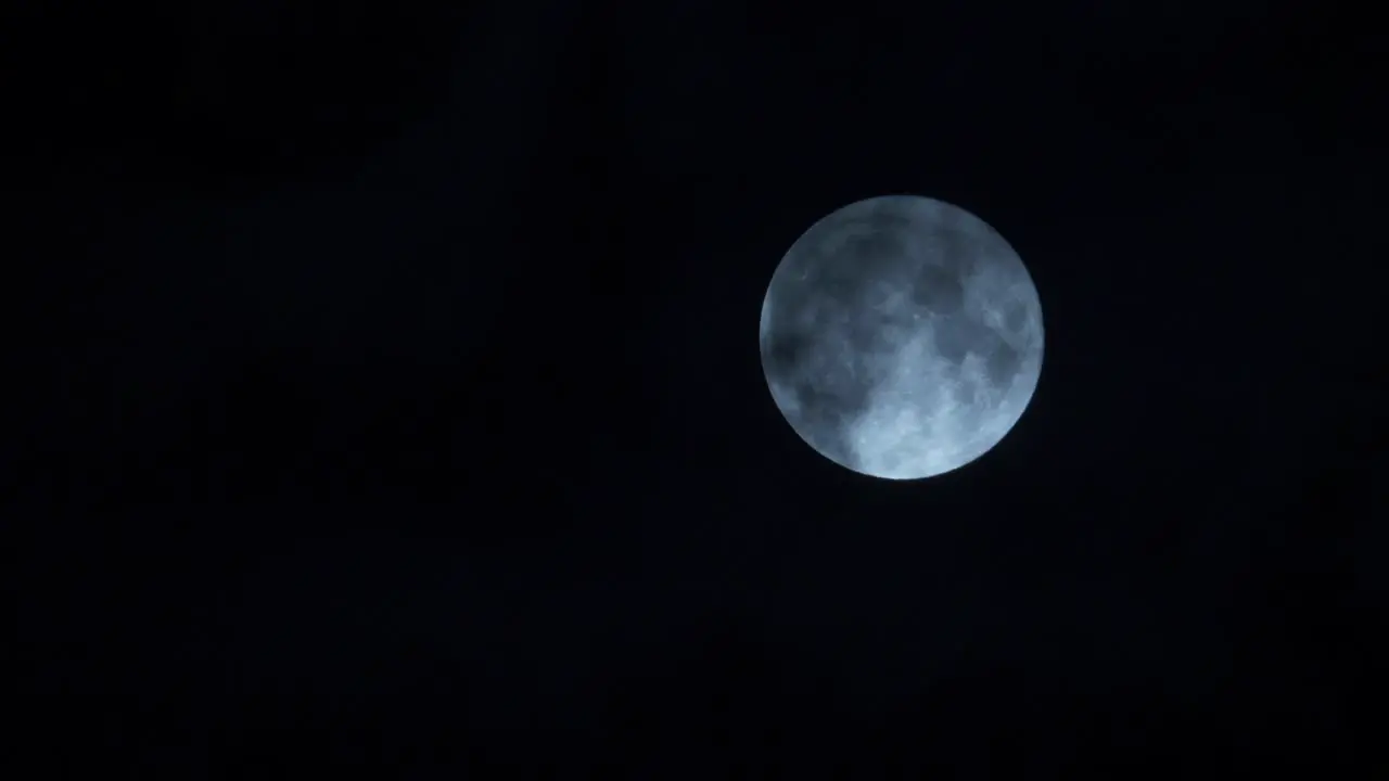 Clouds passing glowing illuminated full moon in dark night sky