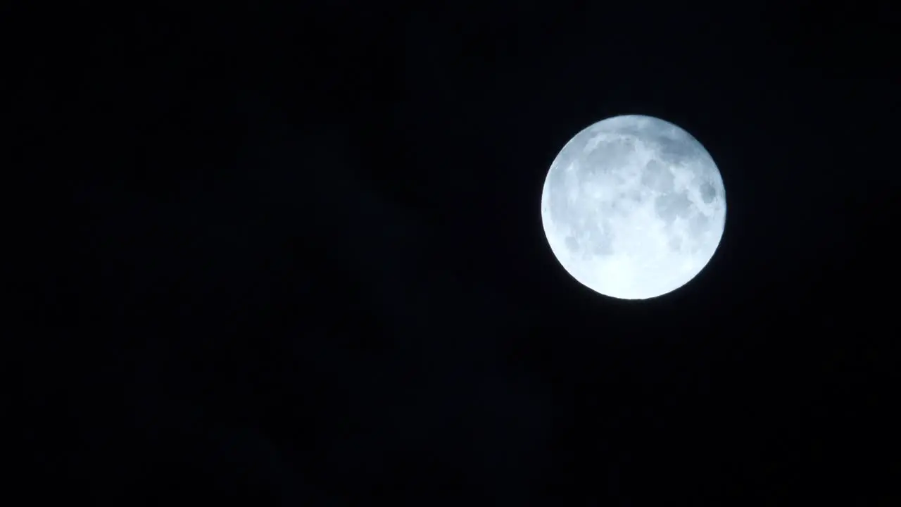 Full moon glowing with clouds moving past blown by wind black background night