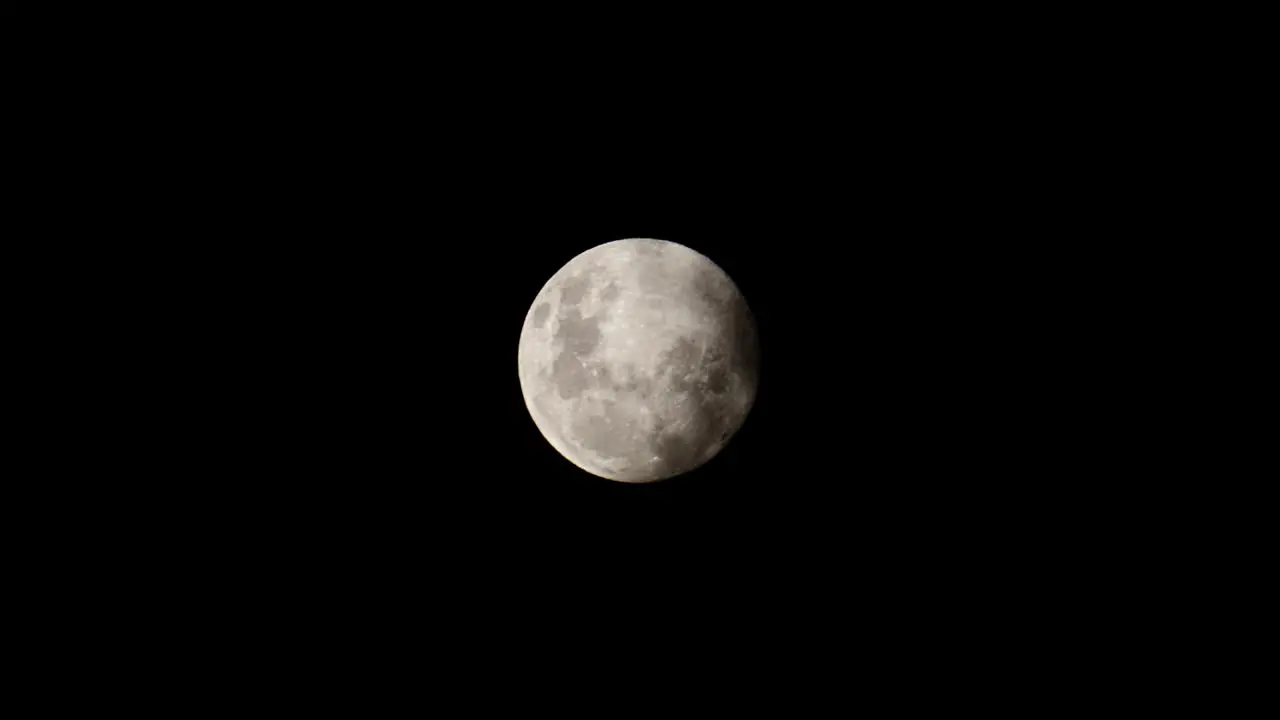 Full moon against black sky slowly appears from behind clouds