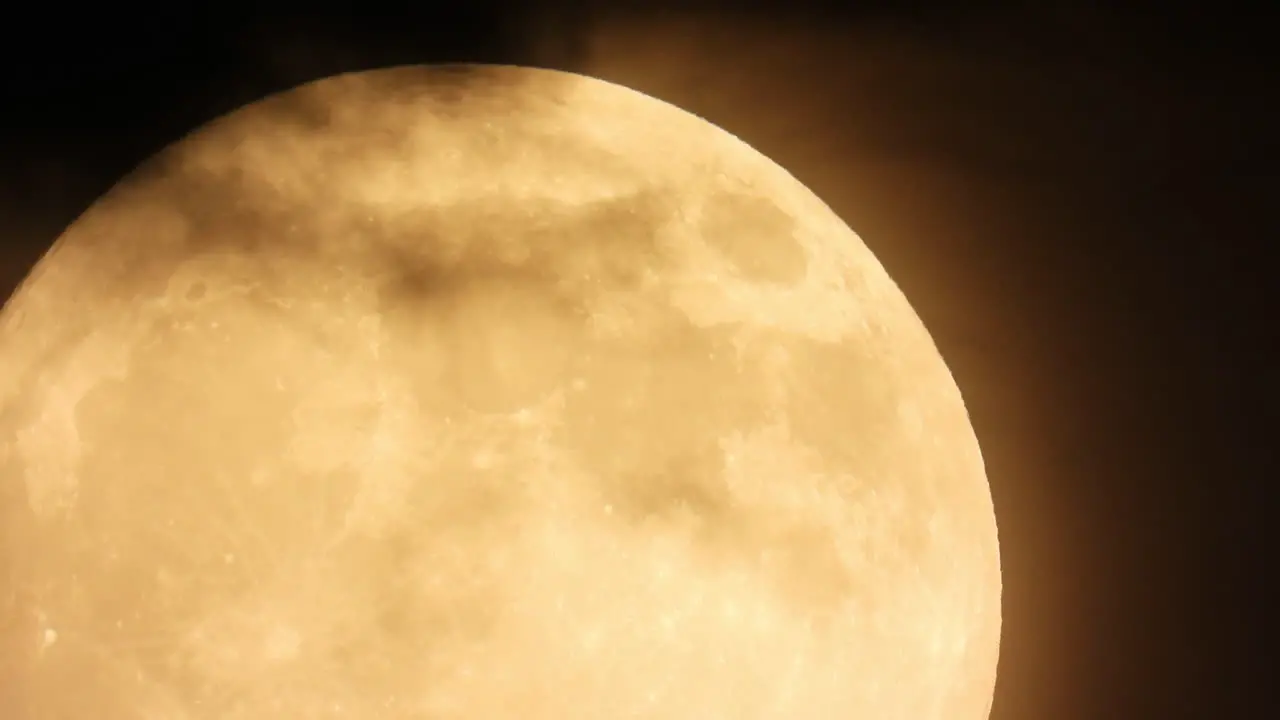 Dark clouds move past a bright orange full moon