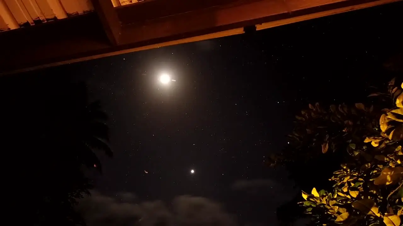 The moon caught on time lapse with clouds and stars moving across the sky from the terrace of a hawaiian home