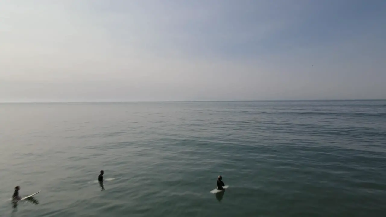 A done shot skimming over the ocean surf away from the shore towards surfers sitting waiting for a wave