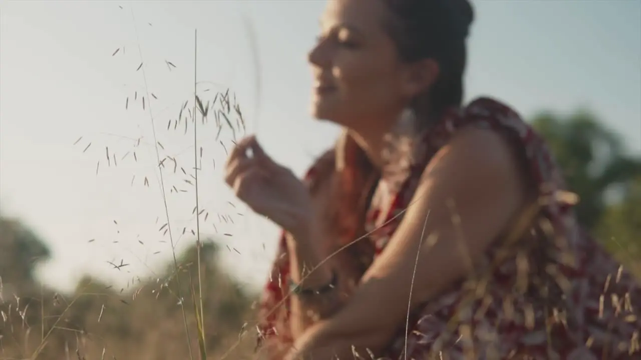 Blurred woman wearing a dress smiling and playing with plants in the field during the day