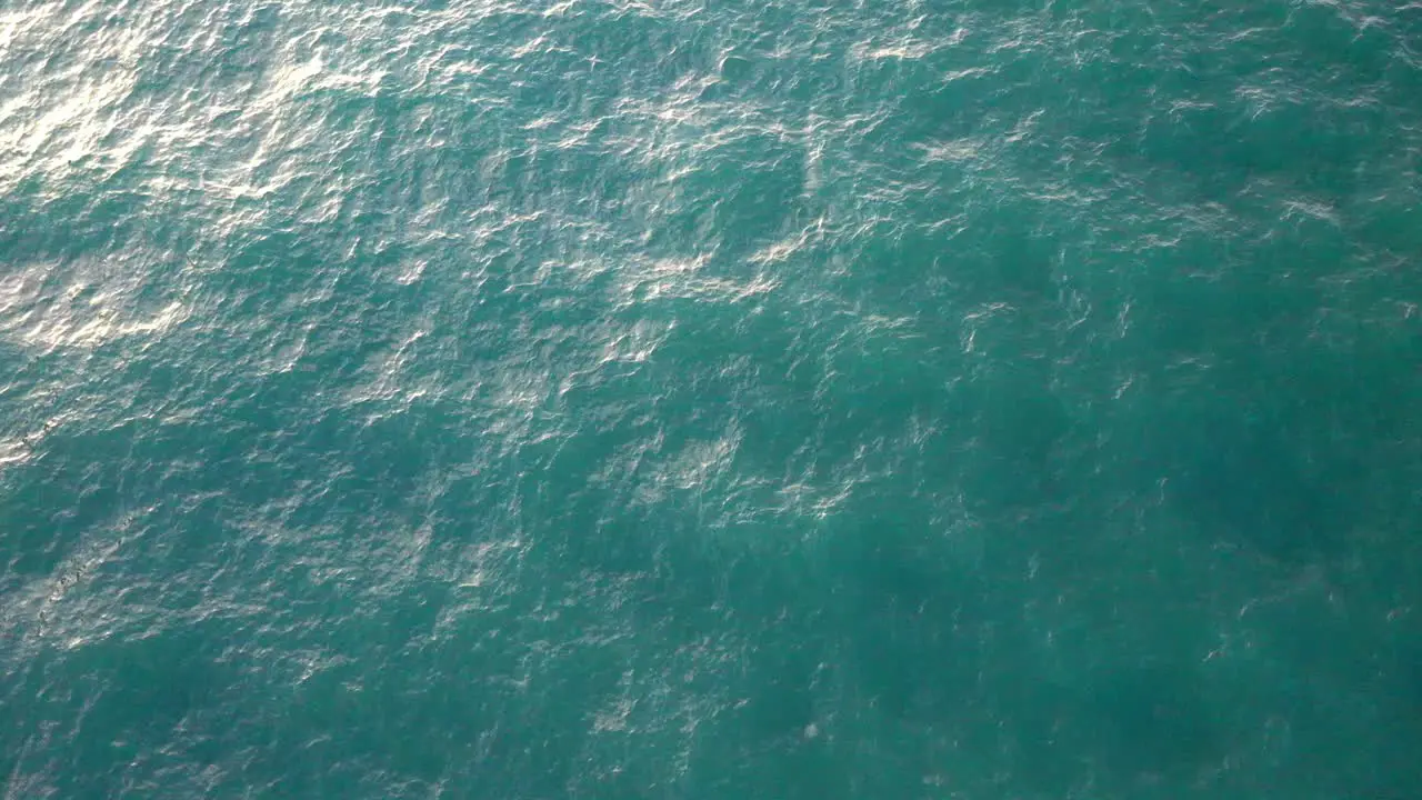 top view of waves in a calm blue sea with the sun reflecting