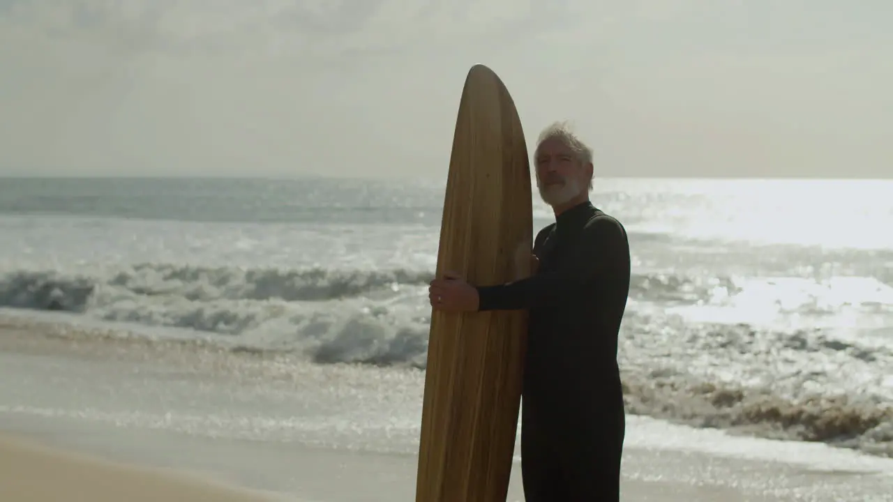 Senior Man With Surfboard Standing On The Sandy Beach And Dreaming