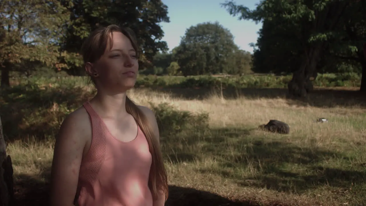 A young woman taking deep breathe under the shade of tree with sun's ray falling on her face