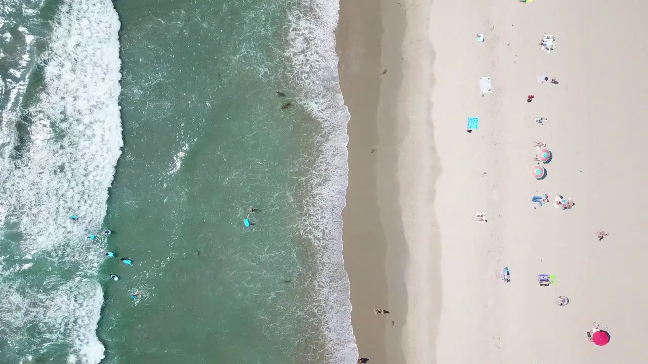 Birdseye sunny golden sandy beach aerial view above shimmering turquoise green Pacific ocean