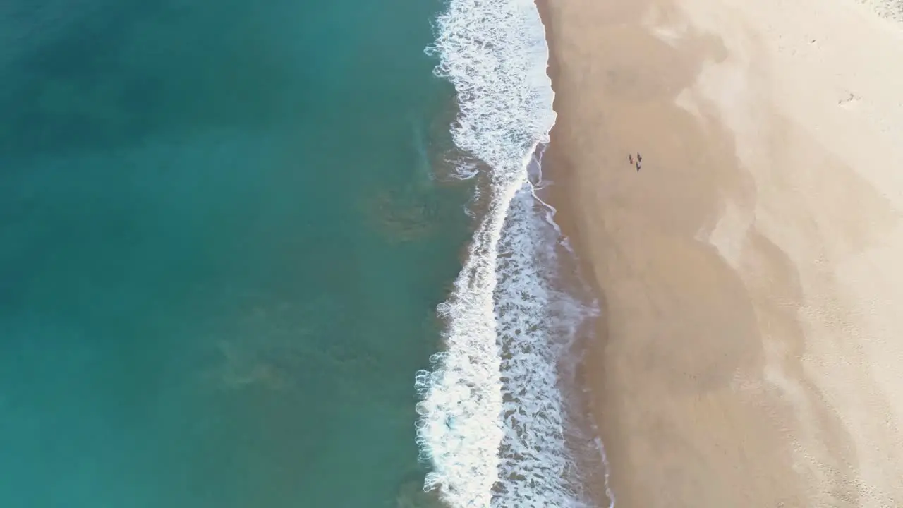 Aerial view of the waves of the blue sea breaking on the sand of a beautiful long white sand beach and some white houses in the distance